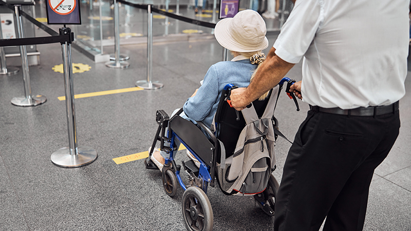 Rear view of airport worker pushing man on wheelchair in the airplane. Concept of traveling with special needs.