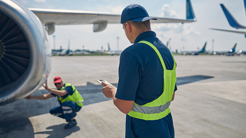 Rear view of airport worker pushing man on wheelchair in the airplane. Concept of traveling with special needs.